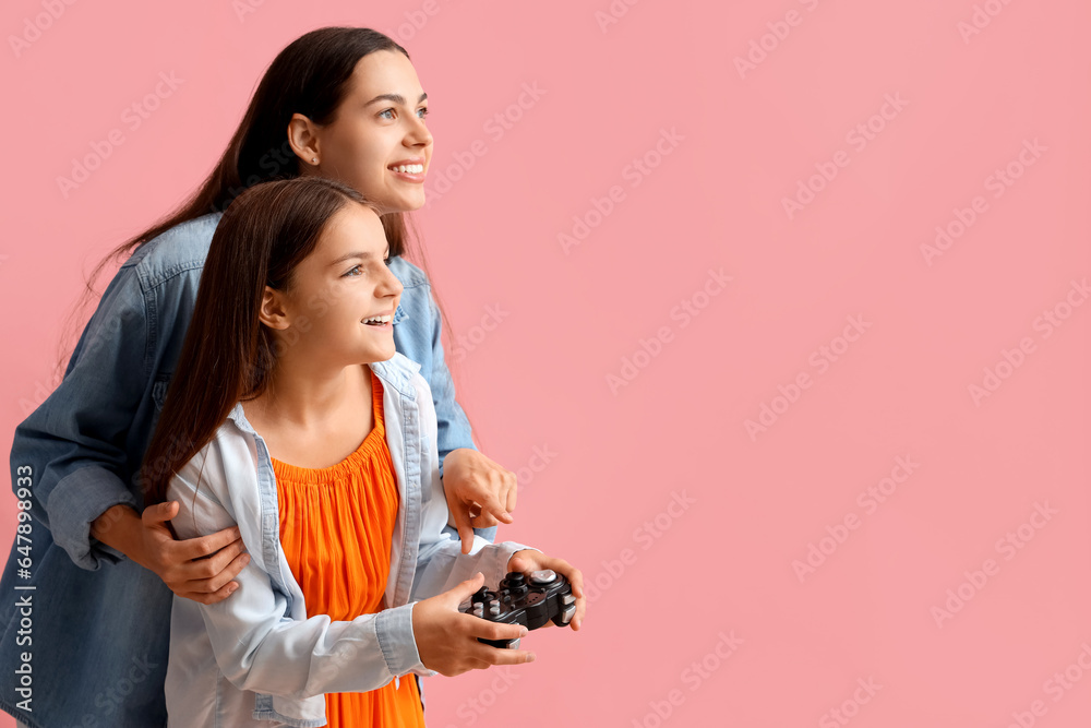 Happy mother and her little daughter with game pad on pink background - obrazy, fototapety, plakaty 