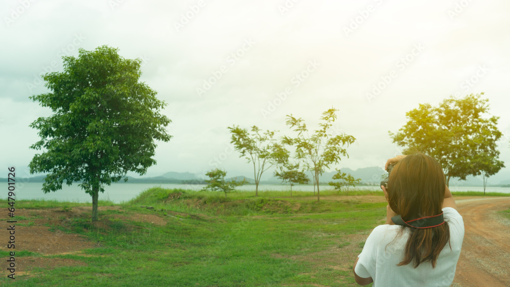 Young asia girl with her back turned taking a photo with her digital camera to nature of Morning Reservoir surface. Travelers lifestyle and natural in Rayong Thailand. Young asia girl with her back turned taking a photo with her digital camera to nature of Morning Reservoir surface. Travelers lifestyle and natural in Rayong Thailand.