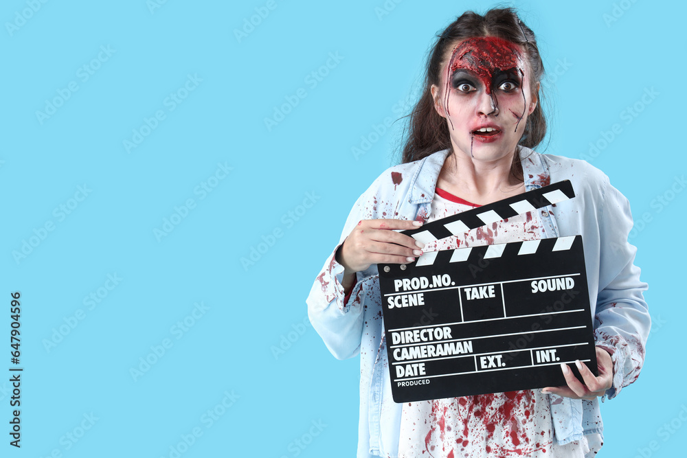 Young woman dressed for Halloween as zombie with movie clapper on blue background