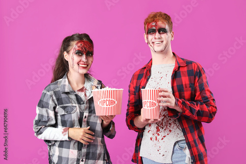 Young couple dressed for Halloween with popcorn on pink background