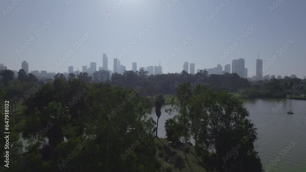 Revealing the Tel Aviv towers behind the trees of Yarkon Park (Yehoshua Gardens), a huge stretch of greenery in the center of Tel Aviv for picnic, rent a bike, rent a boat, water park and playgrounds Revealing the Tel Aviv towers behind the trees of Yarkon Park (Yehoshua Gardens), a huge stretch of greenery in the center of Tel Aviv for picnic, rent a bike, rent a boat, water park and playgrounds