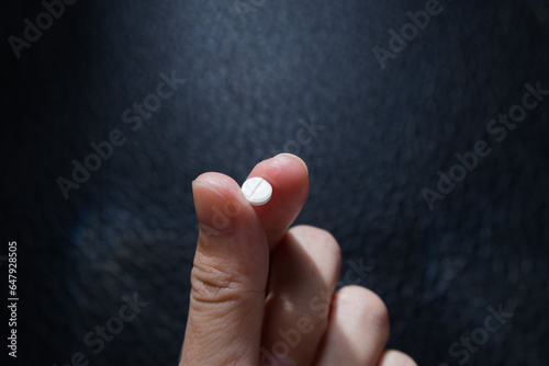 Thyroid treatment pill holding on patient’s hand before taking on textured black background. Synthetic thyroxine, the replacement of thyroid hormone thyroxine.