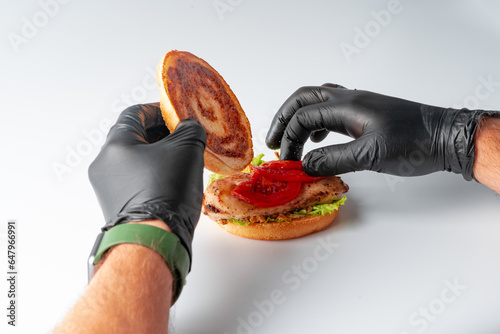 Cook's hands in black gloves making burger on white background photo