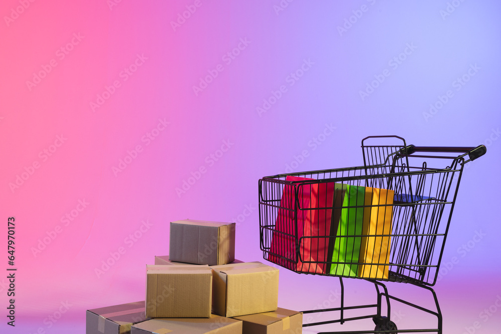 Shopping trolley with bags, boxes and copy space over neon purple background