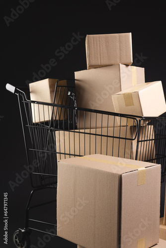Vertical image of shopping trolley with boxes and copy space over black background