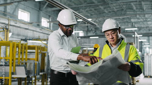 Portrait of nice likeable attractive African-American male wearing white shirt and helmet having a work talk conversation with cute graceful Asian man in safety hardhat.