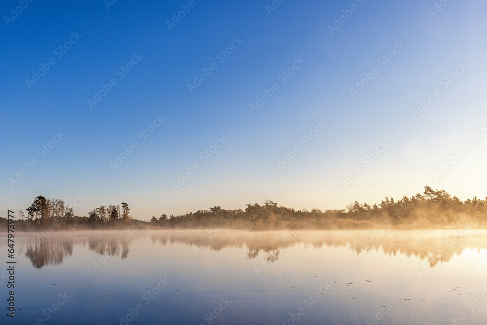 Beautiful autumn morning by a forest lake with fog and mirror-like water