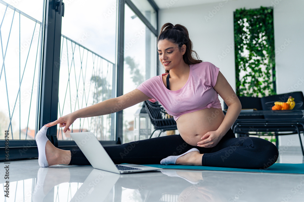 © DusanJelicic - sporty pregnant woman sit on mat meditate practice yoga with online class on computer at home.