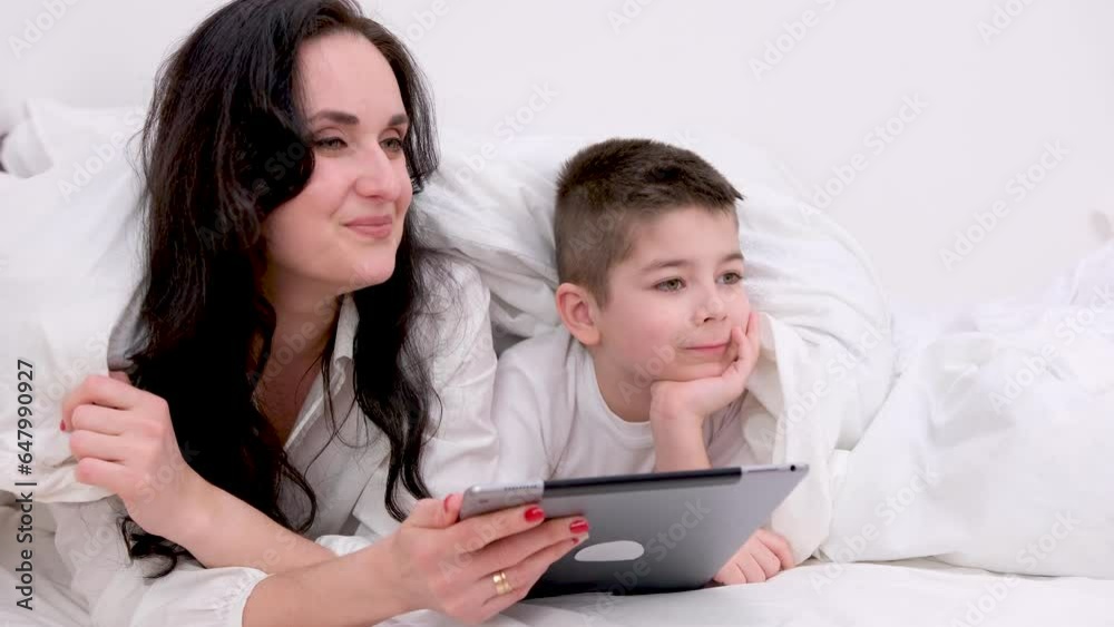 mom and son under blanket playing on tablet boy 4-6 years old woman with black hair beautiful lies under white sheet press buttons laugh smile games internet online learning educational activities mom and son under blanket playing on tablet boy 4-6 years old woman with black hair beautiful lies under white sheet press buttons laugh smile games internet online learning educational activities