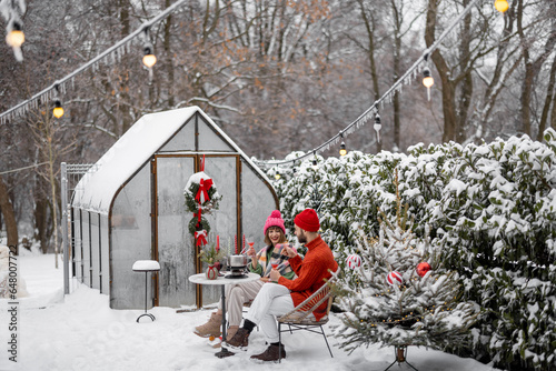 Man and woman have romantic dinner, while sitting together by the table at beautifully decorated snowy backyard. Young family celebrating winter holidays photo