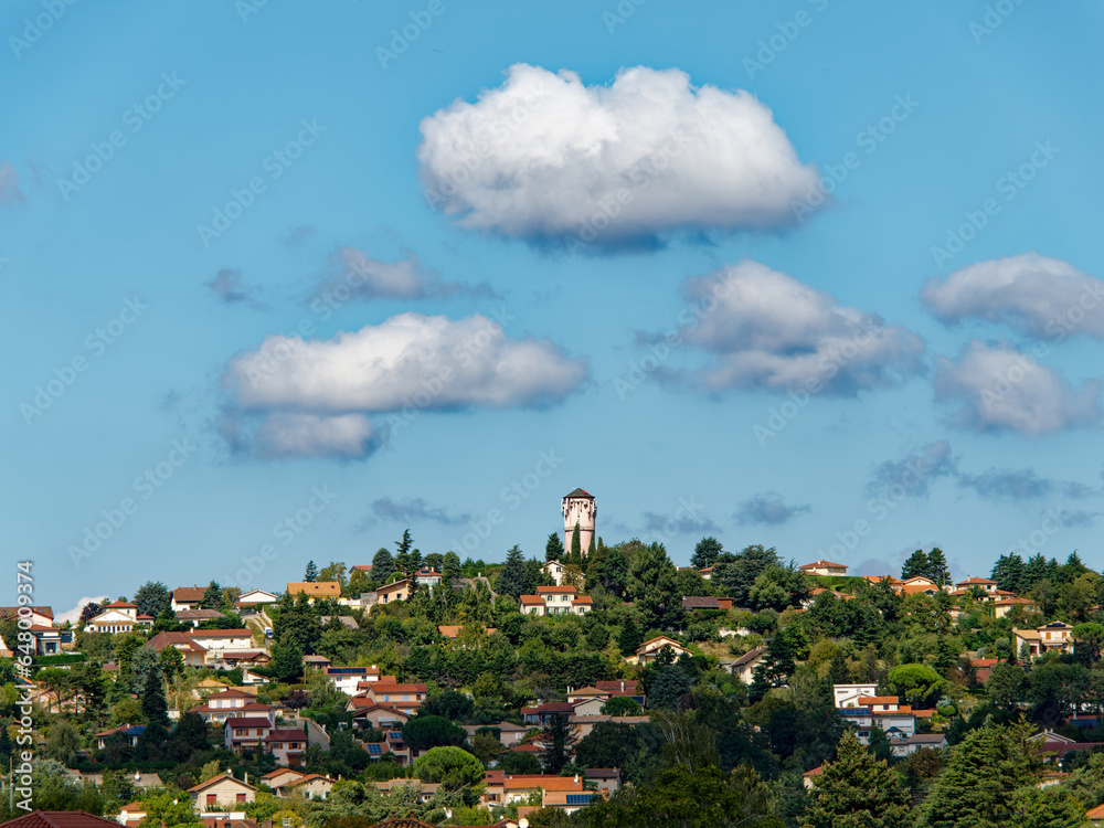 Fototapeta premium View of the city of Communay and its iconic water tower, a sunny day with scattered clouds, France