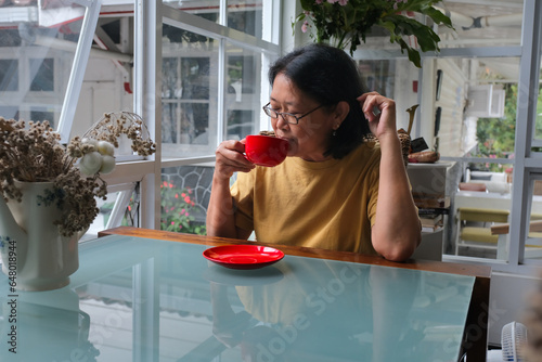 Woman sitting in her dining table drinking a cup of coffee in red ceramic cup photo