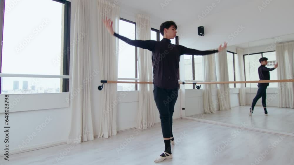 Young Hispanic male dancer practicing classical ballet movements with graceful arms and good posture in modern studio with barre and glass wall Young Hispanic male dancer practicing classical ballet movements with graceful arms and good posture in modern studio with barre and glass wall