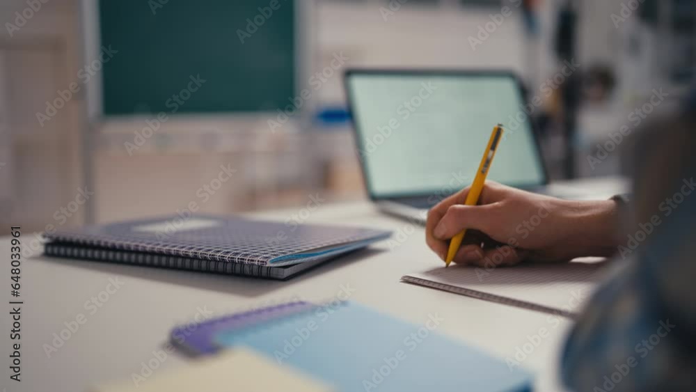 Closeup of a pupil writing in a notebook in the classroom, studying in school