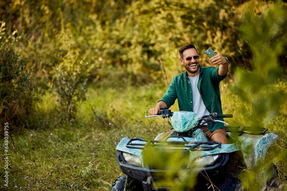 A man having an adventure driving a quad bike and taking a selfie with his phone.