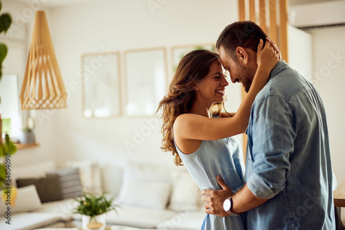 Fotografie A romantic couple in love hugging before kissing while standing in the living room