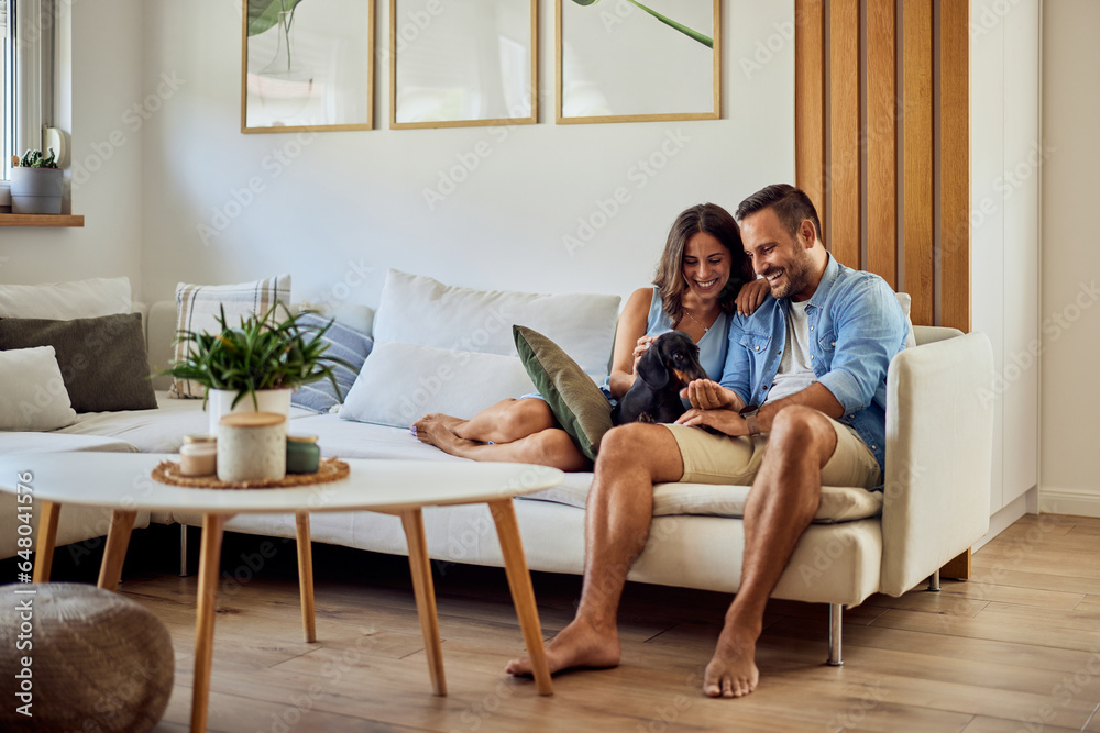 Obraz premium A smiling love couple cuddling their cute little dachshund dog at home.