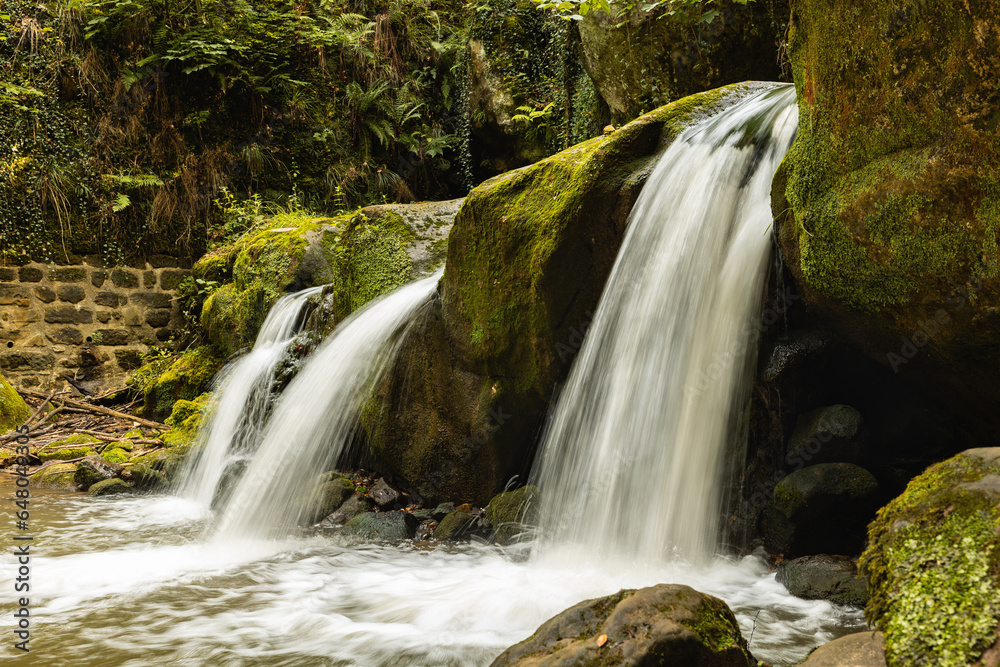Obraz premium Schiessentümpel waterfall in the hills of Mullerthal, Luxembourg. The Black Ernz river flows through the valley. Summer, green moss, forest.