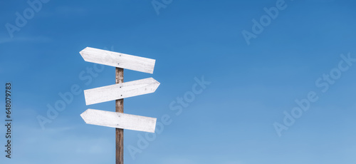 Blank wooden sign against the sky. Direction signpost on a blue horizontal background. The right path and wrong way. Guidance concept. © Win Nondakowit
