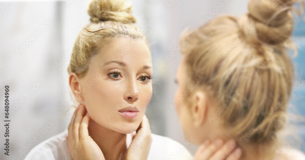 woman looking in the mirror in the bathroom and taking care of her skin.