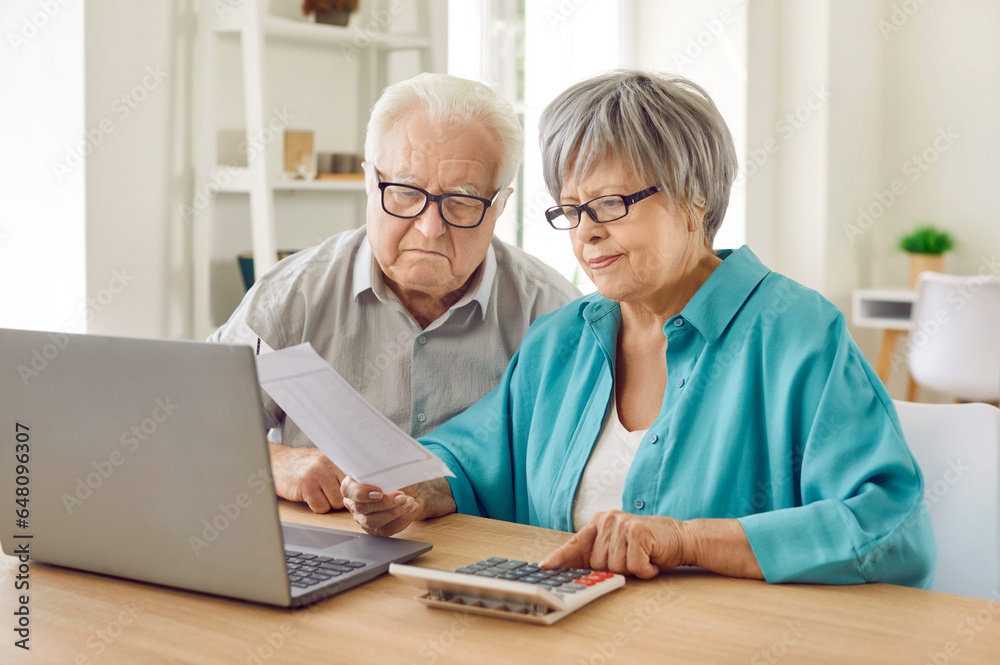 Senior couple sitting at the table and calculating finances or taxes at home. Elderly retired man and woman checking utility bills, counting income and profit. Pension calculation concept. Senior couple sitting at the table and calculating finances or taxes at home. Elderly retired man and woman checking utility bills, counting income and profit. Pension calculation concept.