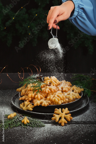 A woman's hand sprinkles powdered sugar on a sweet treat brushwood in the form of snowflakes photo