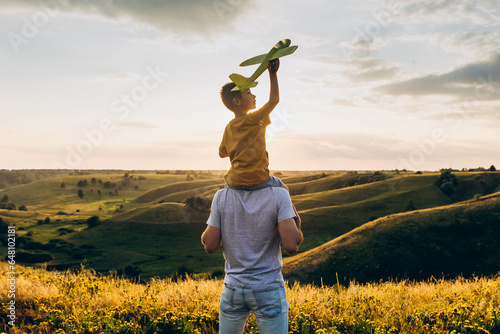 Dad and son playing together outdoors with yellow plane. Father and son launch a toy airplane at sunset. Happy family. Father's Day.