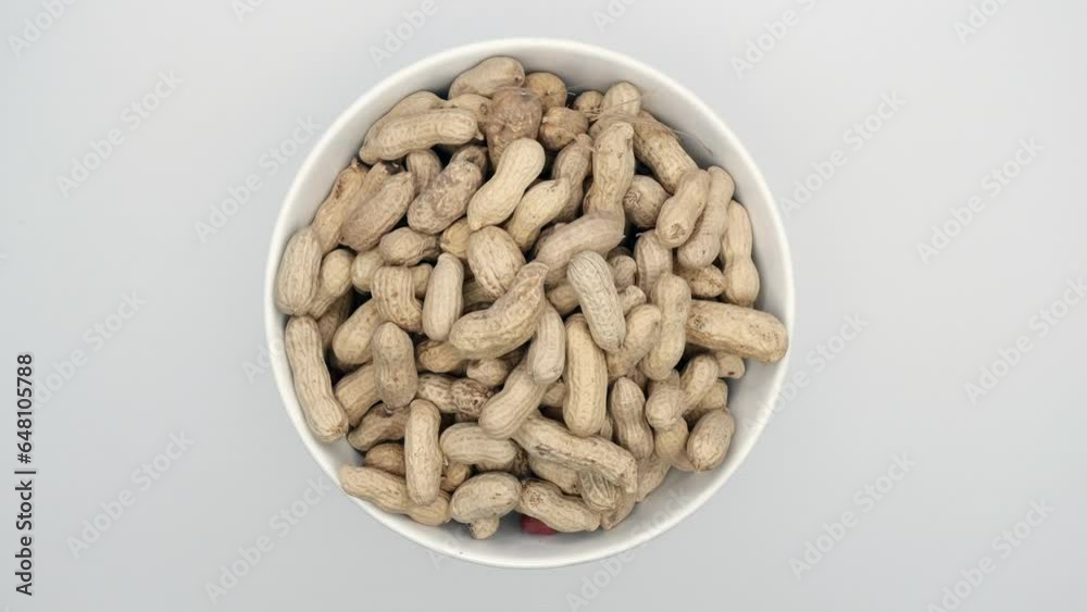 Raw Peanuts With Shells In White Bowl On White Background. Rotating. Close Up. Top View. Raw Peanuts With Shells In White Bowl On White Background. Rotating. Close Up. Top View.
