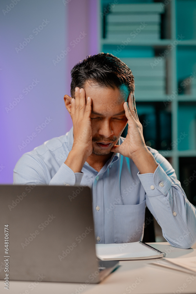 Asian man showing tired and stressed expression in the office, company employee working overtime, working late at night, working overtime of a busy and hard working company employee. Overtime concept. Asian man showing tired and stressed expression in the office, company employee working overtime, working late at night, working overtime of a busy and hard working company employee. Overtime concept.