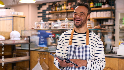 Smiling Man With Down Syndrome Working In Food Shop Using Digital Tablet