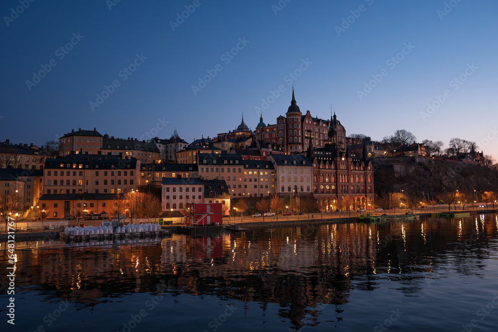 Old buildings with their lights in central Stockholm at dusk, overlooking the lake, on a calm winter day.