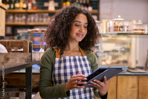 Smiling Young Woman Wearing Apron Working In Food Shop Using Digital Tablet