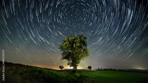 Time lapse of the night sky on a rural landscape with star trails and cloud motion effect