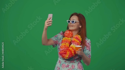 Woman traveller in glasses and flower wreath having a video call on smartphone, happy face. Isolated on green background.