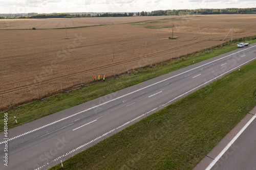 Drone photography of construction workers building a fence between a high intensity highway and a wheat field © M