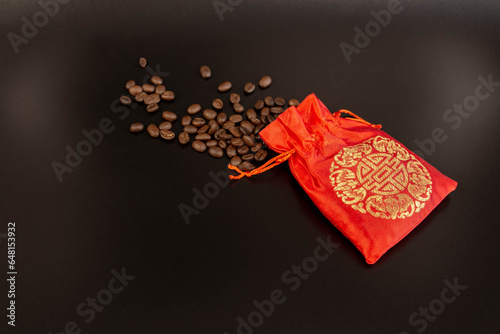 Coffee beans spilled from a red silk bag close-up with black background