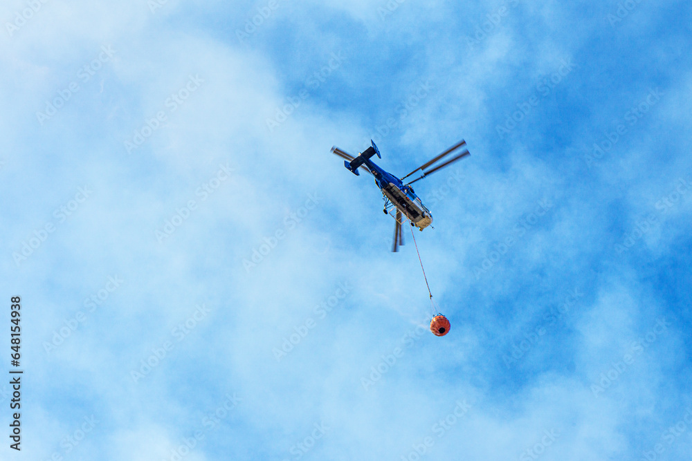 tragic view of forest fire and helibucket which is a specialized bucket suspended on a cable carried by a helicopter to deliver water for aerial firefighting tragic view of forest fire and helibucket which is a specialized bucket suspended on a cable carried by a helicopter to deliver water for aerial firefighting