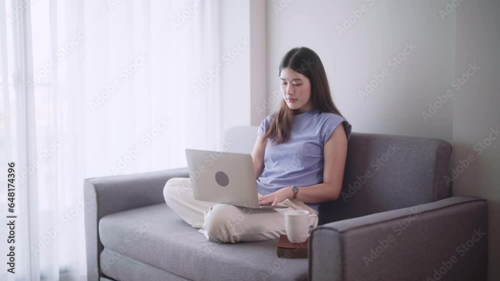 Pretty Asian woman surfing social media or working on laptop while lying on the sofa when relax in living room at home., Concept of activity in living room. Pretty Asian woman surfing social media or working on laptop while lying on the sofa when relax in living room at home., Concept of activity in living room.