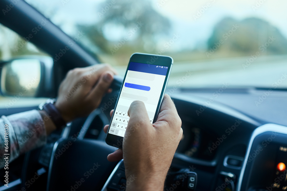 Young man texting on his smartphone while driving his car in the city