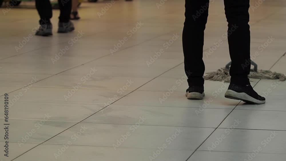 A slow-motion shot of cleaning woman washing the floor in a mall, people walking around. Woman works as a cleaner in a public place. A slow-motion shot of cleaning woman washing the floor in a mall, people walking around. Woman works as a cleaner in a public place.