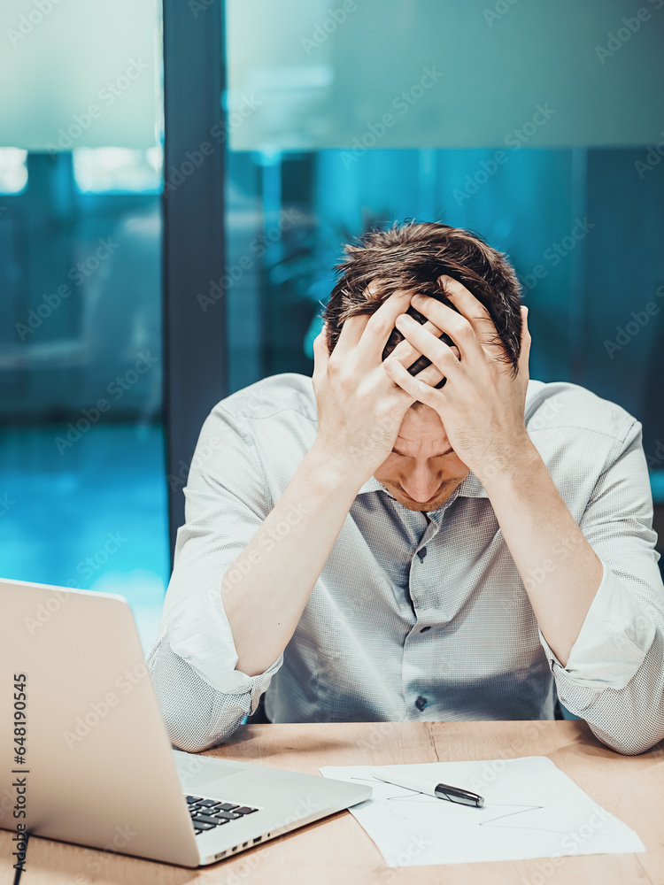 Office worker sits at table and holds his head in his hands. Depression and crisis in workplace. Oppressed worker. Portrait of depressed and frustrated analyst. Office worker sits at table and holds his head in his hands. Depression and crisis in workplace. Oppressed worker. Portrait of depressed and frustrated analyst.