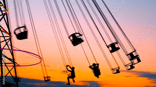 Unrecognizable silhouettes of people ride on the chained carousel against the warm evenning sky at sunset with at amusement park. Entertainment, summer, fun and holiday concept