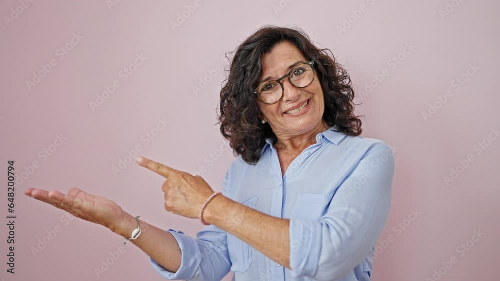 Middle age hispanic woman smiling pointing to the side presenting over isolated pink background