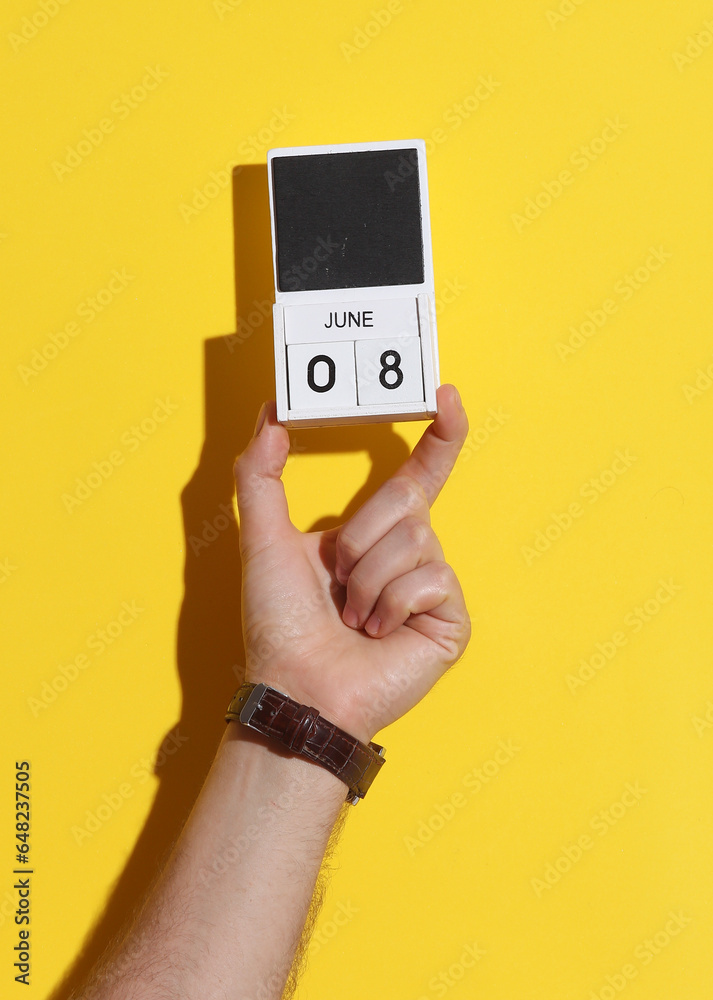 Man's hand holding wooden block calendar with date June 8 on yellow background Man's hand holding wooden block calendar with date June 8 on yellow background