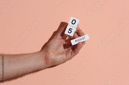 Man's hand holding wooden block calendar with date august 5 on pink bright background photo