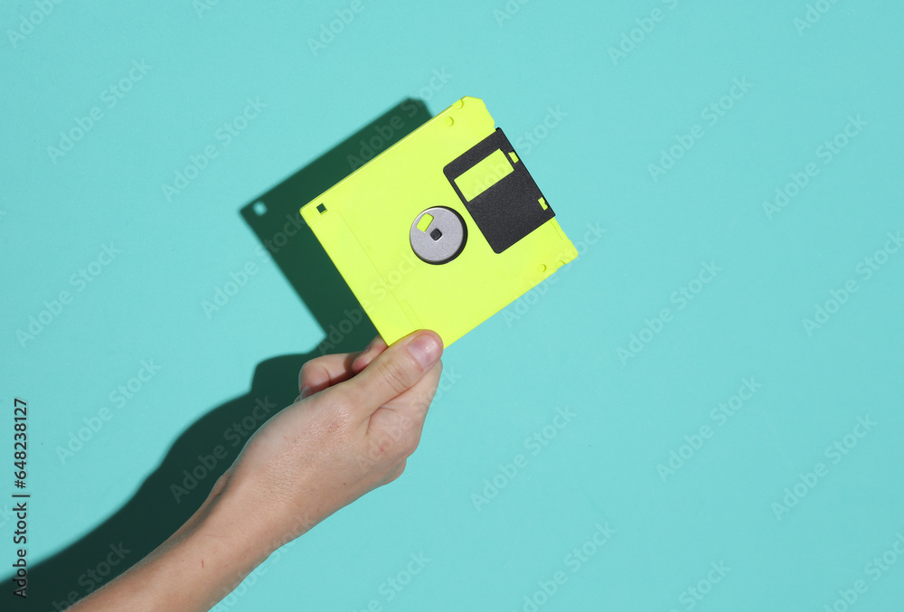 © splitov27 - Hand holding a yellow retro 80s floppy disk on a blue background