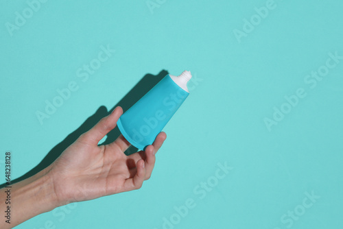 Woman's hand holds blue tube of cream on a blue background