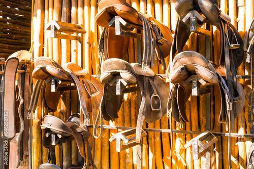 Photos Leather horse bridles and bits hanging on a wooden wall of stable at a horse farm