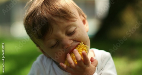Cute baby eating corn cob outside. Portrait of infant toddler boy taking a bite of corn food photo