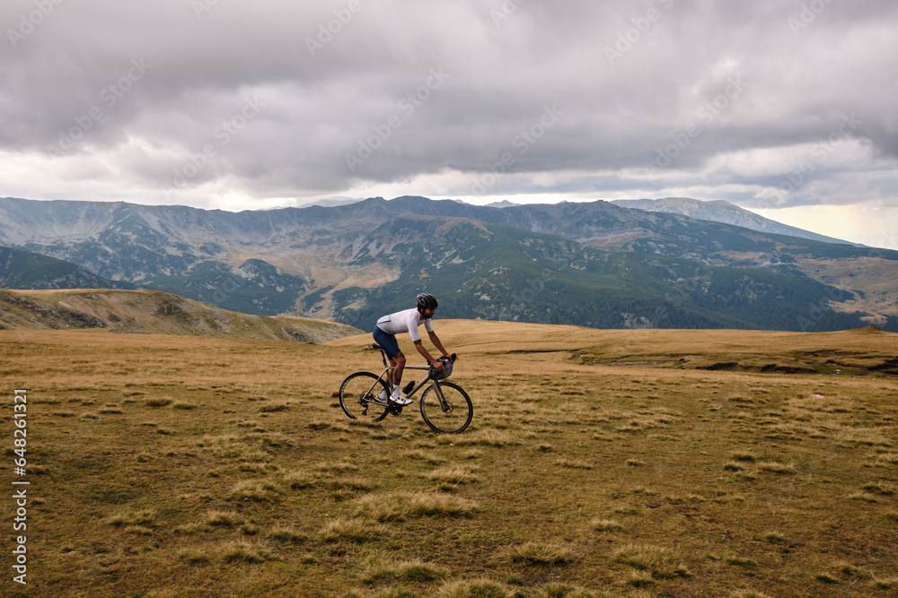 Fit male cyclist riding dirt trails on a gravel bike.Man riding a gravel bike on gravel road with beautiful view on mountains.Sports motivation.Gravel road in mountains.Bikepacking concept.Transalpina